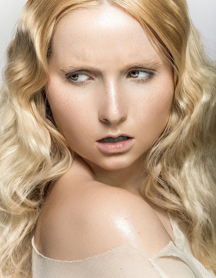 Close-up of a woman with wavy blonde hair and piercing eyes looking sideways. photographer NYC