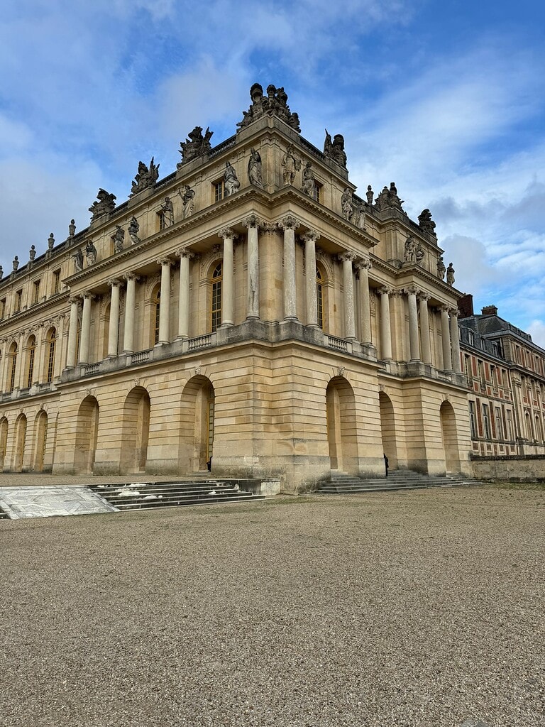 Exterior corner of the Palace of Versailles with stone columns, sculpted figures and blue sky.