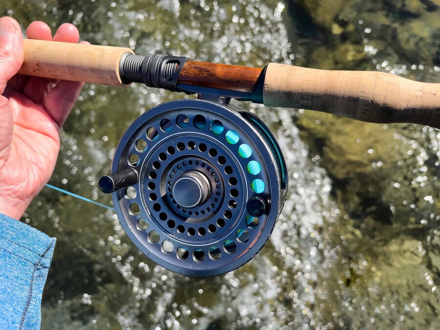 Hand on a fly reel beside fast river water