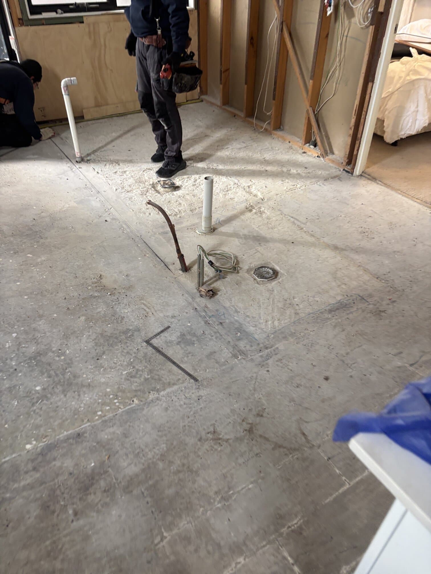 Concrete slab in renovated bathroom with visible damp patch during plumbing inspection.