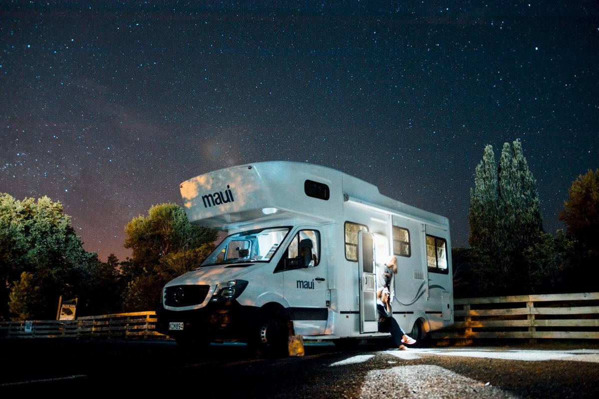 Camper Maui bianco parcheggiato di notte sotto un cielo stellato, persona seduta all’ingresso con laptop acceso