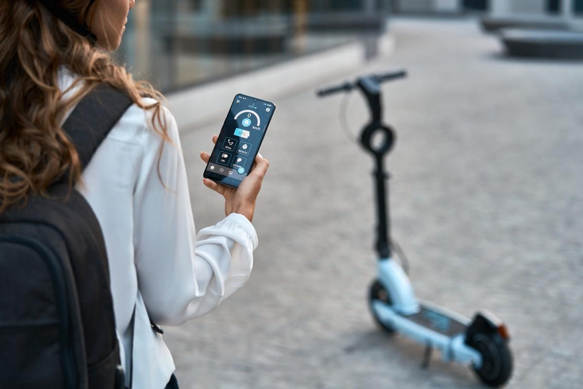 Controllo intelligente di monopattino elettrico tramite app sullo smartphone, con scooter elettrico in background, immagine perfetta per contenuti su mobilità sostenibile e tecnologia vehicle data.