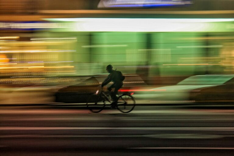 Ciclista su e-bike in movimento notturno con sfondo sfocato e luci dinamiche su strada trafficata