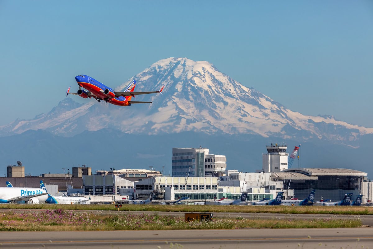 Southwest Boeing in partenza dall'aeroporto di Seattle con lo sfondo del Monte St. Helens innevato, simbolo di avventura e viaggi.