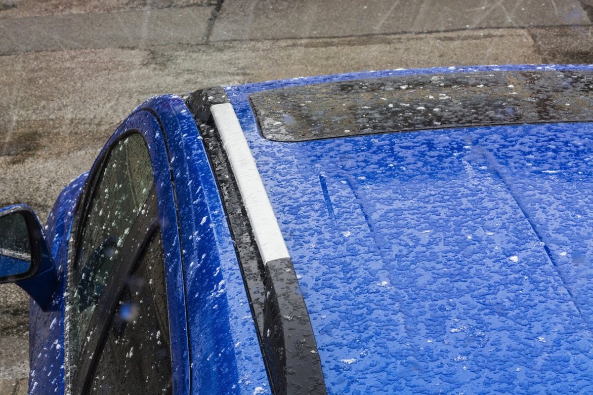 Tetto di un'auto blu danneggiato dalla grandine, vista dall'alto, con gocce e ammaccature evidenti sulla carrozzeria.