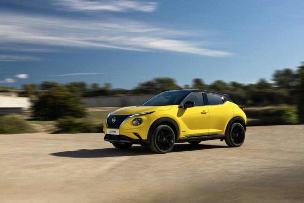 Nissan Juke N-Sport gialla in movimento su strada sterrata con sfondo alberato e cielo limpido.