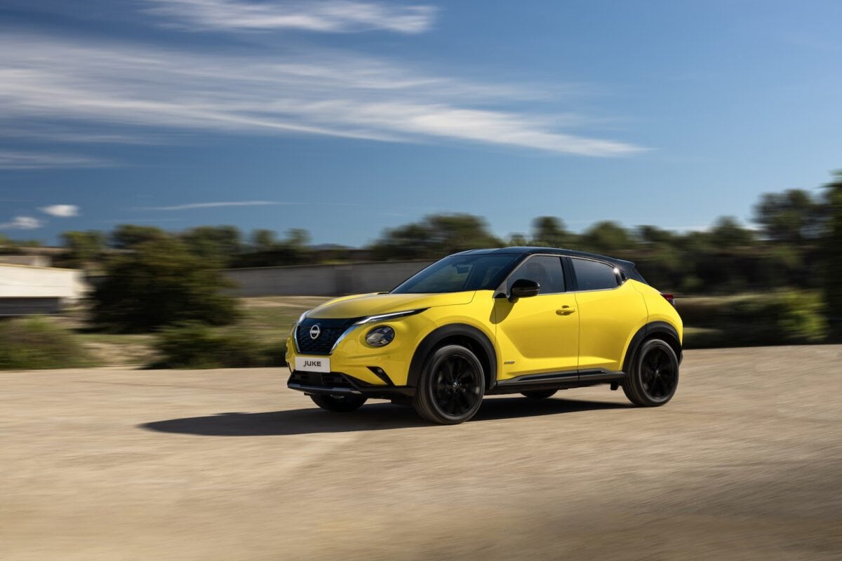 Nissan Juke N-Sport gialla in movimento su strada sterrata con sfondo alberato e cielo limpido.