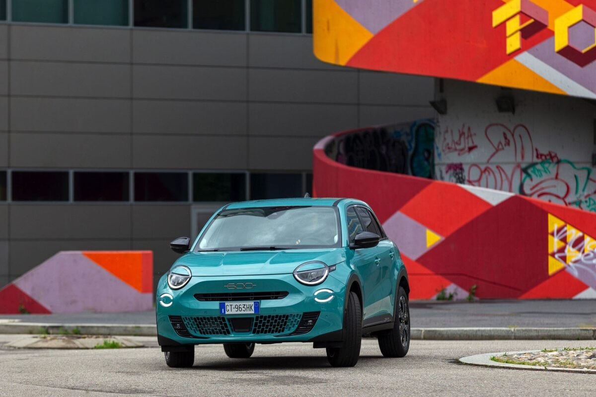 Fiat 600 Hybrid 2024 turchese fotografata in ambiente urbano con murales colorati sullo sfondo.