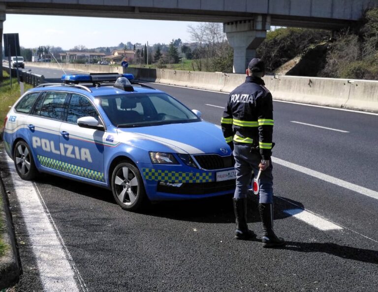 Agente della Polizia Stradale accanto a pattuglia Skoda Octavia, in sosta sulla corsia d’emergenza di un’autostrada sotto cavalcavia.