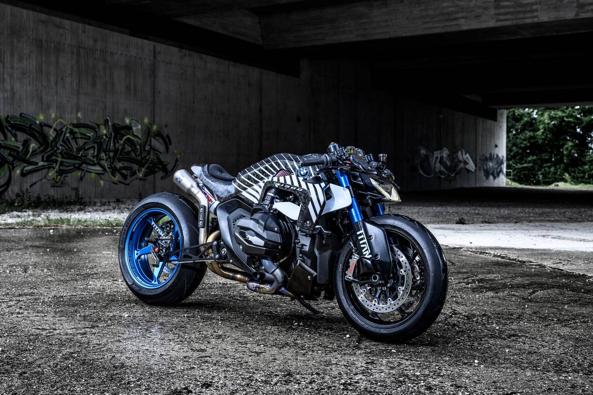 BMW R 1300 R Titan parcheggiata su asfalto bagnato, cerchi blu, grafica racing, dettagli in carbonio, scarico sportivo