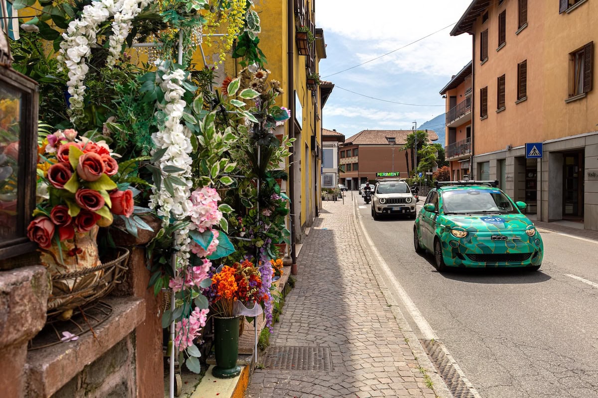 Fiat 500e con livrea del Politecnico di Milano in un centro cittadino con negozio di fiori in primo piano