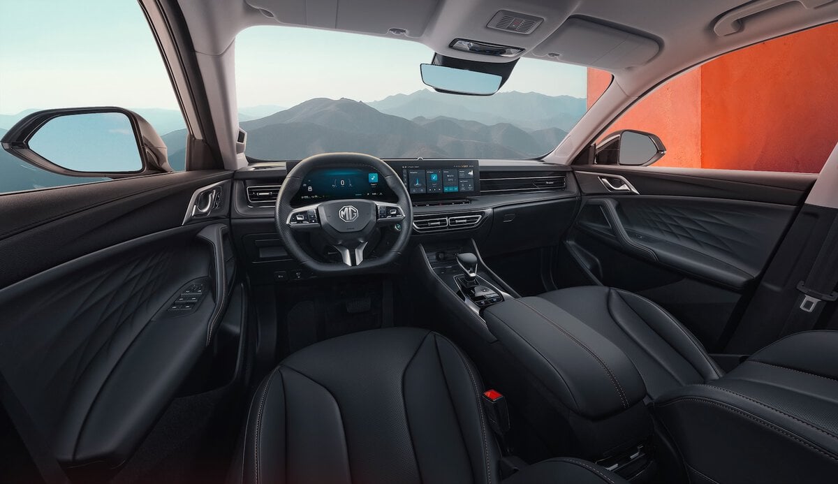 Interni MG HS Hybrid+ con sedili in pelle nera, doppio display digitale e volante multifunzione, vista frontale da posizione guida.