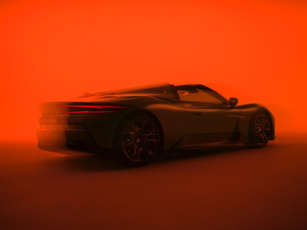 Maserati MCPURA Cielo grigia vista posteriore a 3/4 su sfondo arancione intenso, auto sportiva decappottabile con linee aerodinamiche