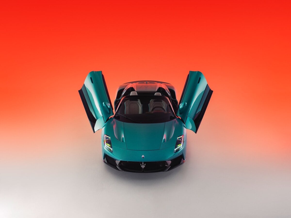 Maserati MCPURA Cielo azzurra vista frontale dall’alto con portiere ad ali di farfalla aperte, su sfondo sfumato arancione