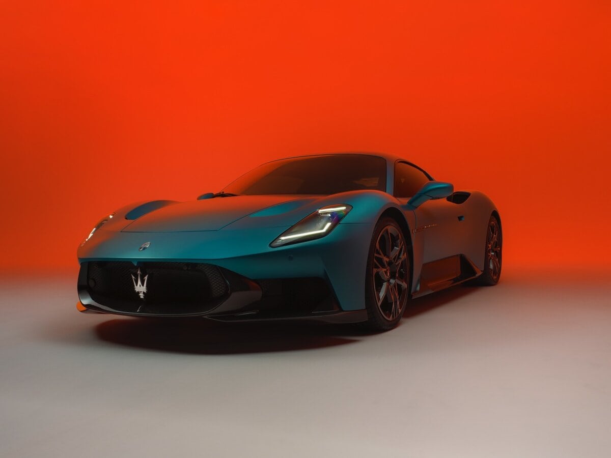 Maserati MCPURA coupé azzurra vista frontale a 3/4 su sfondo arancione, auto sportiva con firma del Tridente