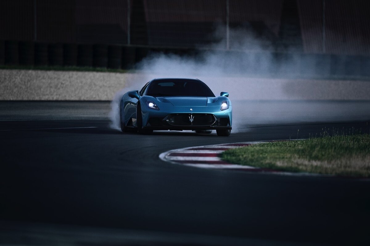Maserati MCPURA coupé azzurra in derapata su pista da corsa, vista frontale con fumo dagli pneumatici in curva