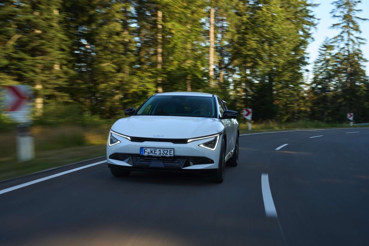 Kia EV6 bianca in movimento su strada curvilinea circondata da alberi in un contesto naturale.