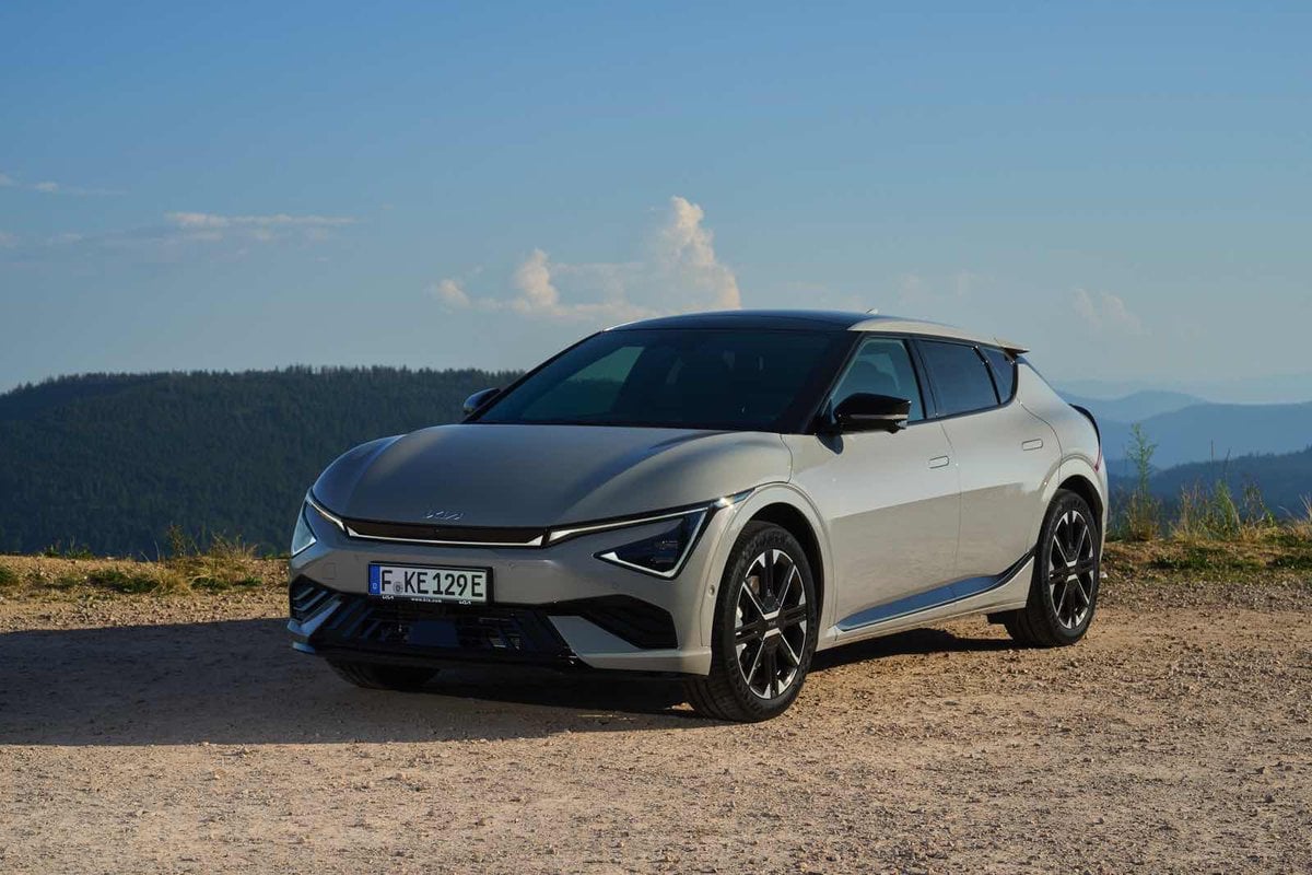 Vista frontale tre quarti della Kia EV6 grigia parcheggiata su sterrato con montagne all’orizzonte.