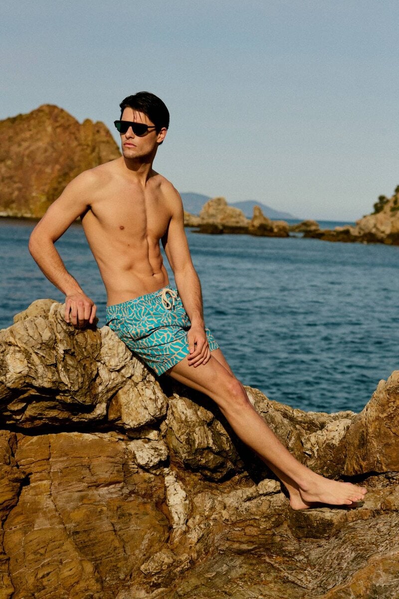 Uomo seduto su scogli con costume turchese Peninsula