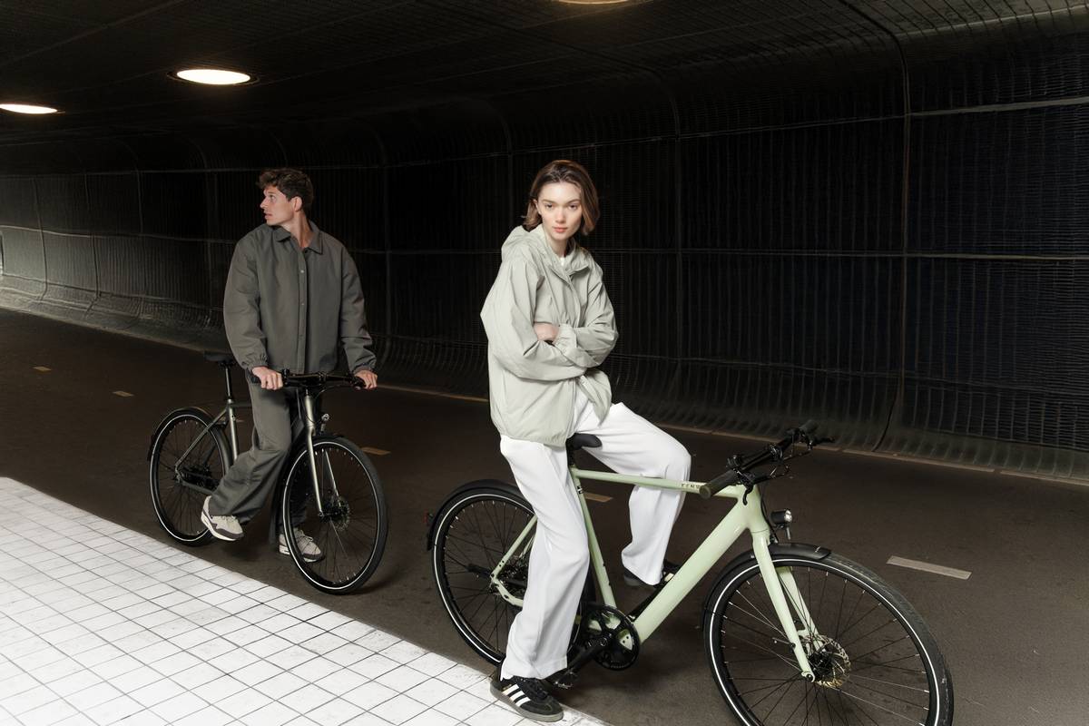 Due biciclette elettriche Tenways CGO600, grigia e verde salvia, design urbano, uomo e donna in tunnel cittadino.