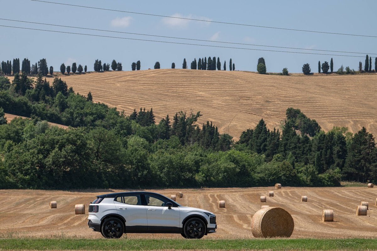 Profilo laterale della Volvo EX30 Cross Country MY26 in sosta su un campo con rotoballe e colline toscane sullo sfondo.