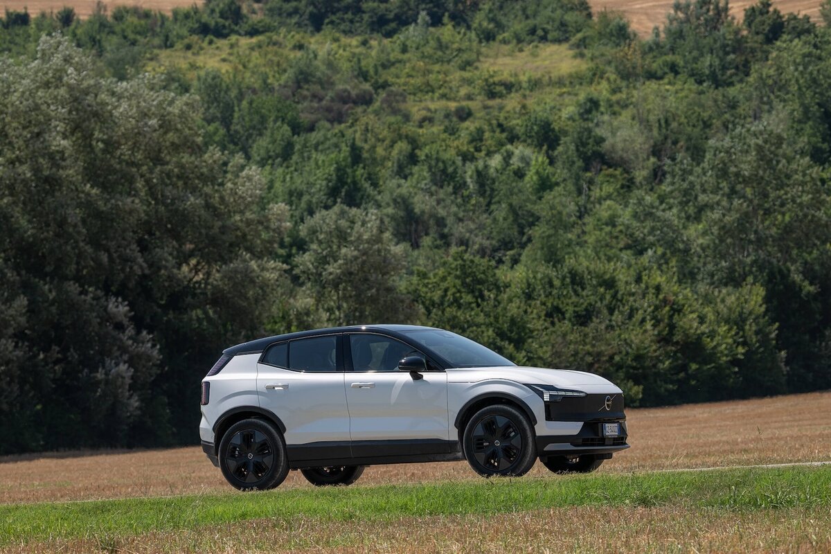 Vista laterale della Volvo EX30 Cross Country 2026 ferma su un prato davanti a un bosco.
