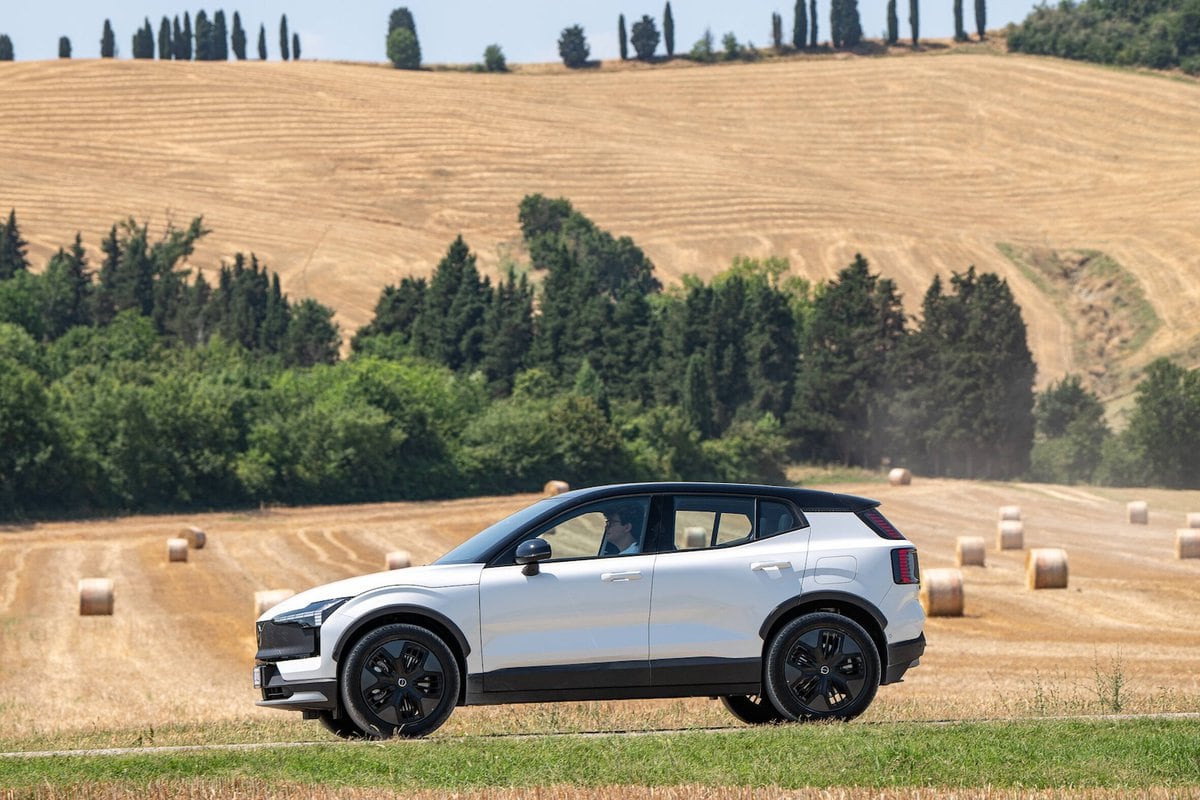Volvo EX30 Cross Country MY26 elettrica ripresa di lato tra le balle di fieno in una tipica ambientazione rurale estiva.