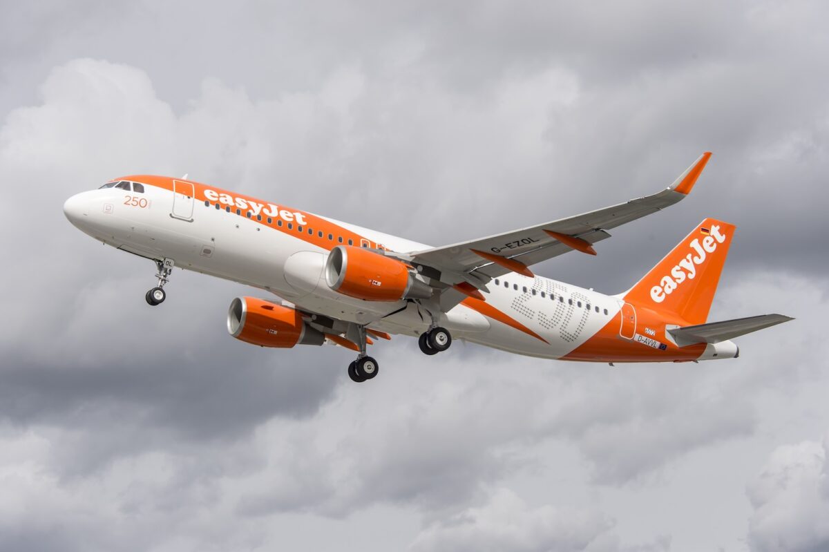 Airbus A320 easyJet in livrea arancione e bianca in fase di decollo, fotografato lateralmente con cielo nuvoloso sullo sfondo.