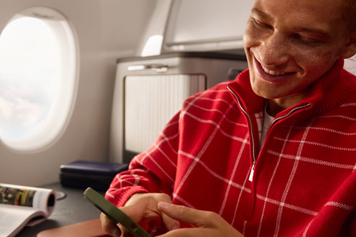 Uomo in felpa rossa controlla il telefono seduto vicino al finestrino durante un volo in classe business.