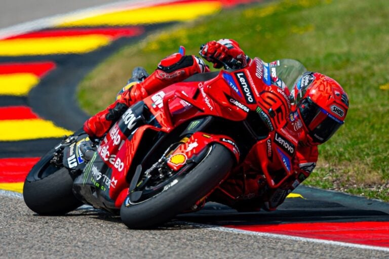 Marc Marquez in piega su Ducati durante il Gran Premio MotoGP 2025 al Sachsenring, con tuta e moto rosse sponsorizzate Lenovo e Monster.