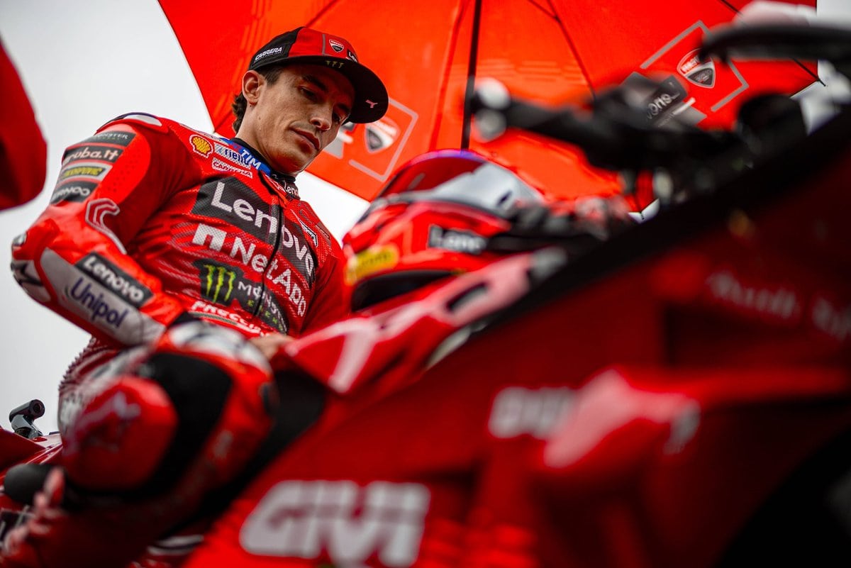 Marc Marquez osserva la sua Ducati nel box prima della gara MotoGP 2025, sotto l’ombrellone ufficiale del team