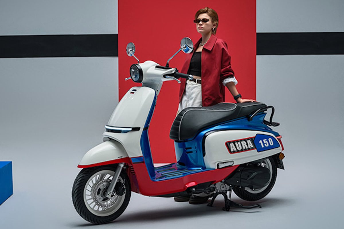 Donna con giacca rossa posa accanto a scooter Aura 150.