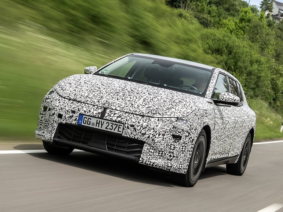 Il prototipo della Kia EV4 completamente camuffato durante i test su strada, ripreso frontalmente mentre percorre una strada panoramica. Il camouflage nasconde i dettagli del design della futura berlina elettrica.