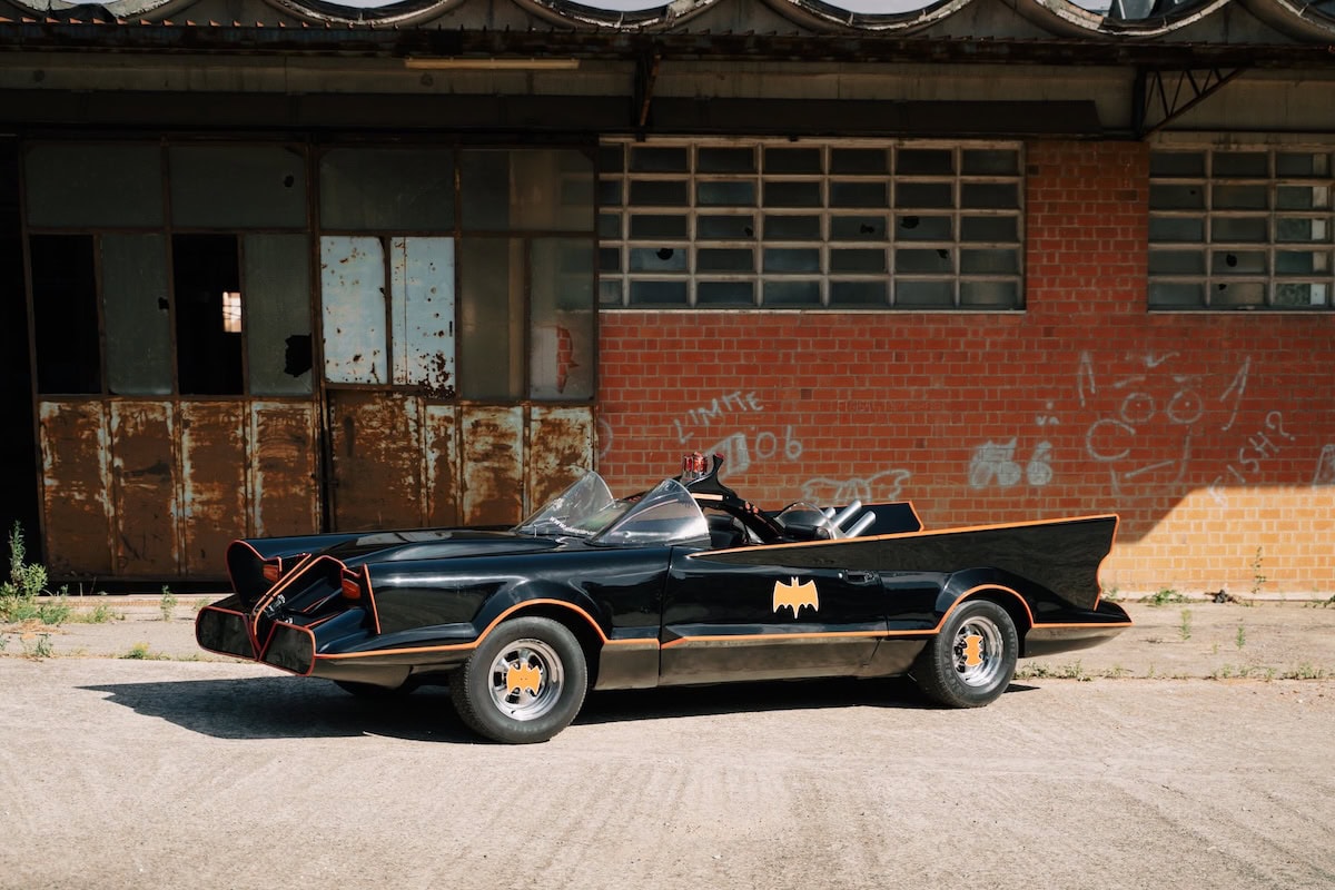 Replica della Batmobile classica nera con bordi arancioni parcheggiata davanti a un edificio industriale.