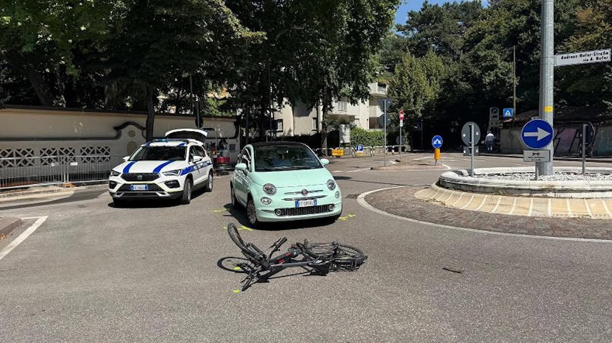 Bicicletta a terra dopo incidente con Fiat 500 in una rotatoria, auto della polizia municipale sul posto.