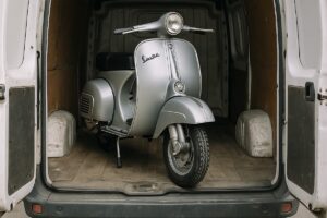 Vespa d'epoca color argento caricata all'interno di un furgone bianco con portellone aperto.
