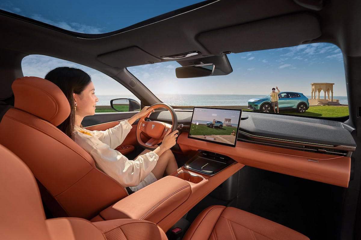 Interni moderni del Deepal S05 con sedili in pelle arancio e cruscotto digitale, guidatrice al volante in riva al mare.