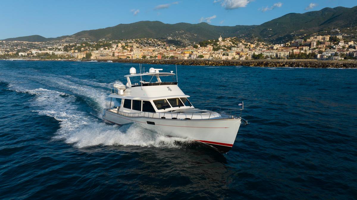 Lussuoso yacht bianco in navigazione nel mare con sfondo di città e montagne.