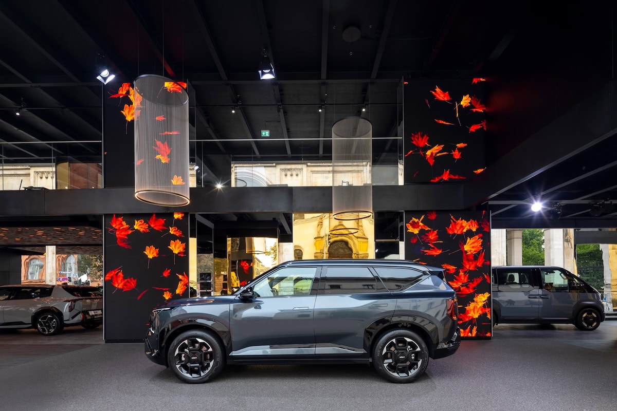 Kia EV5 esposto allo IAA Mobility di Monaco, tra decorazioni luminose con foglie rosse e pannelli a specchio.