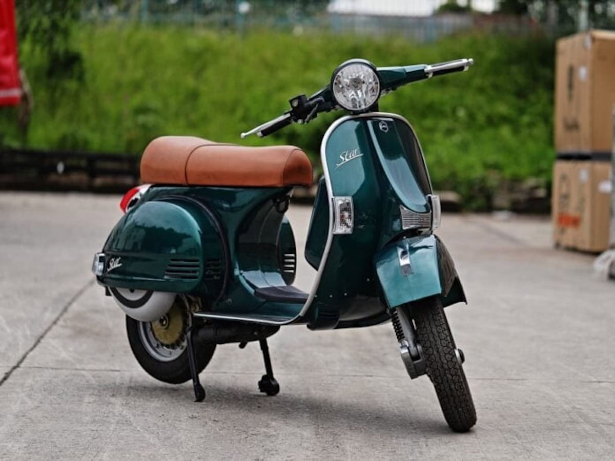 Vespa vintage verde scuro con sedile in pelle marrone, motoscooter classico italiano, stile retrò, motore a due tempi, icona del design motociclistico, veicolo urbano elegante e vintage.