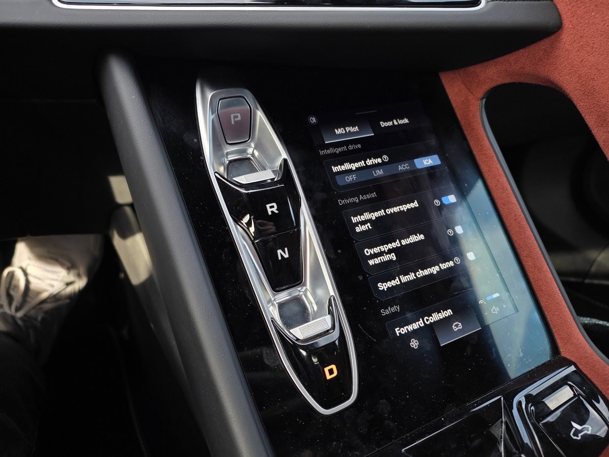 Il selettore di marcia della MG Cyberster GT con schermo digitale dell'auto, interfaccia di controllo della guida e funzioni di assistenza ancora visibili.