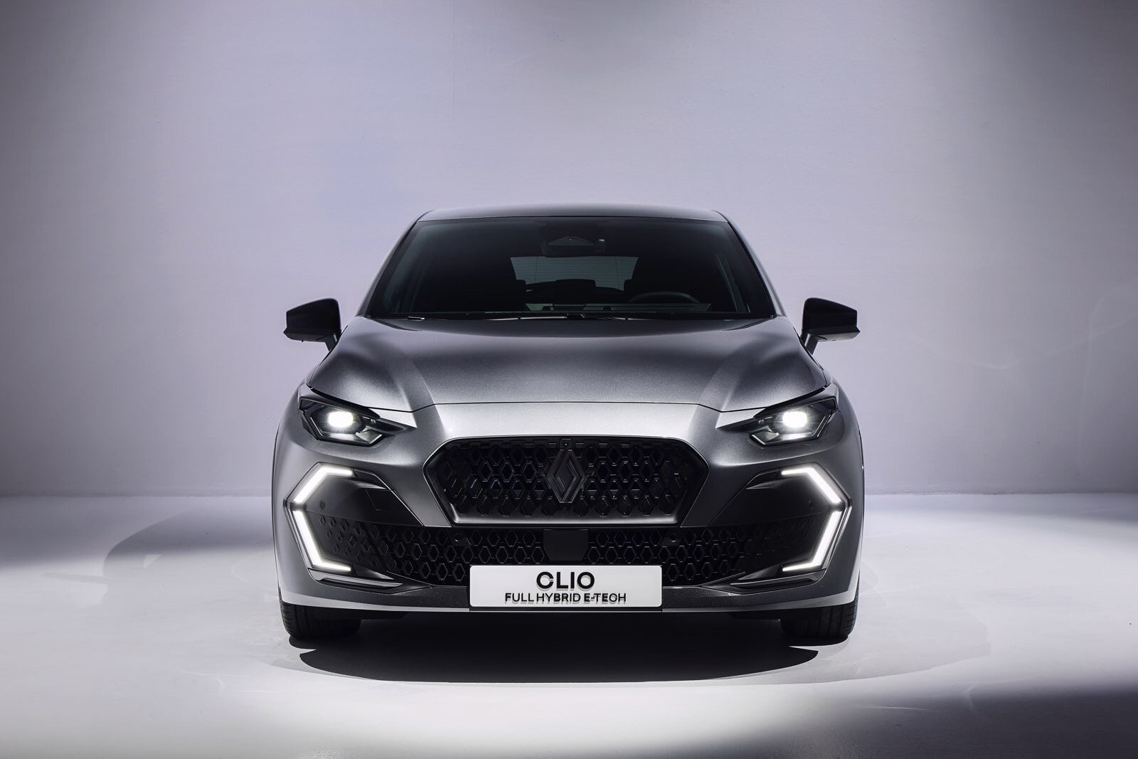 Vista frontale della Renault Clio E-Tech Full Hybrid con luci diurne a LED accese, griglia nera a nido d’ape e design aggressivo.