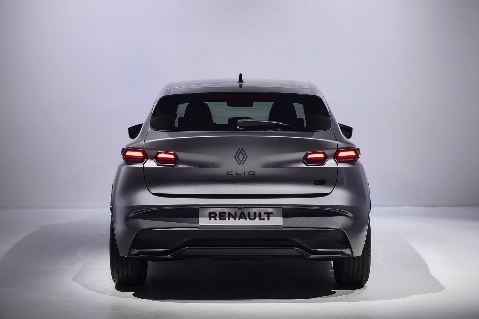 Vista posteriore della Renault Clio E-Tech con firma luminosa LED, nuovo logo centrale e badge Clio visibile su portellone grigio satinato.