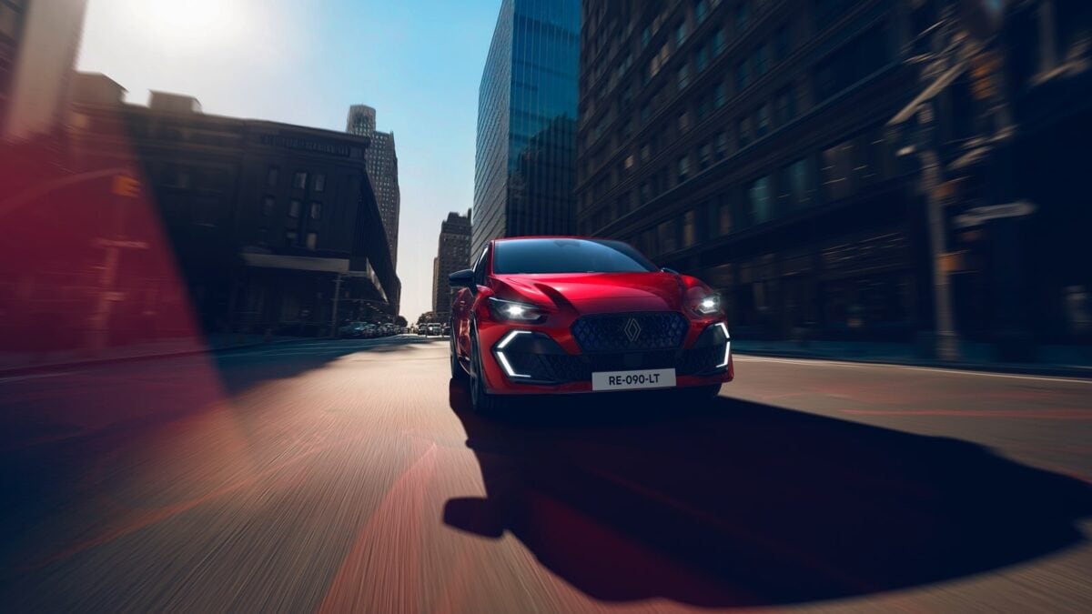 Renault Clio E-Tech rossa fotografata frontalmente mentre corre su una strada cittadina tra grattacieli, con luci LED accese e assetto sportivo.