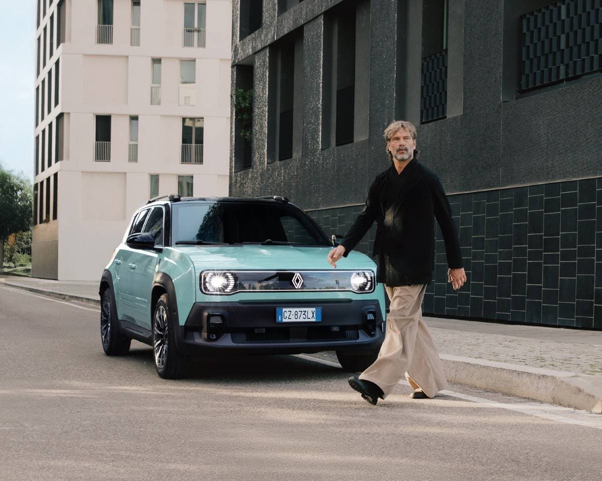 Auto elettrica Renault 5, modello compatto e sostenibile, in una scena urbana moderna. Uomo elegante attraversa la strada accanto al veicolo, simbolo di innovazione e mobilità green.