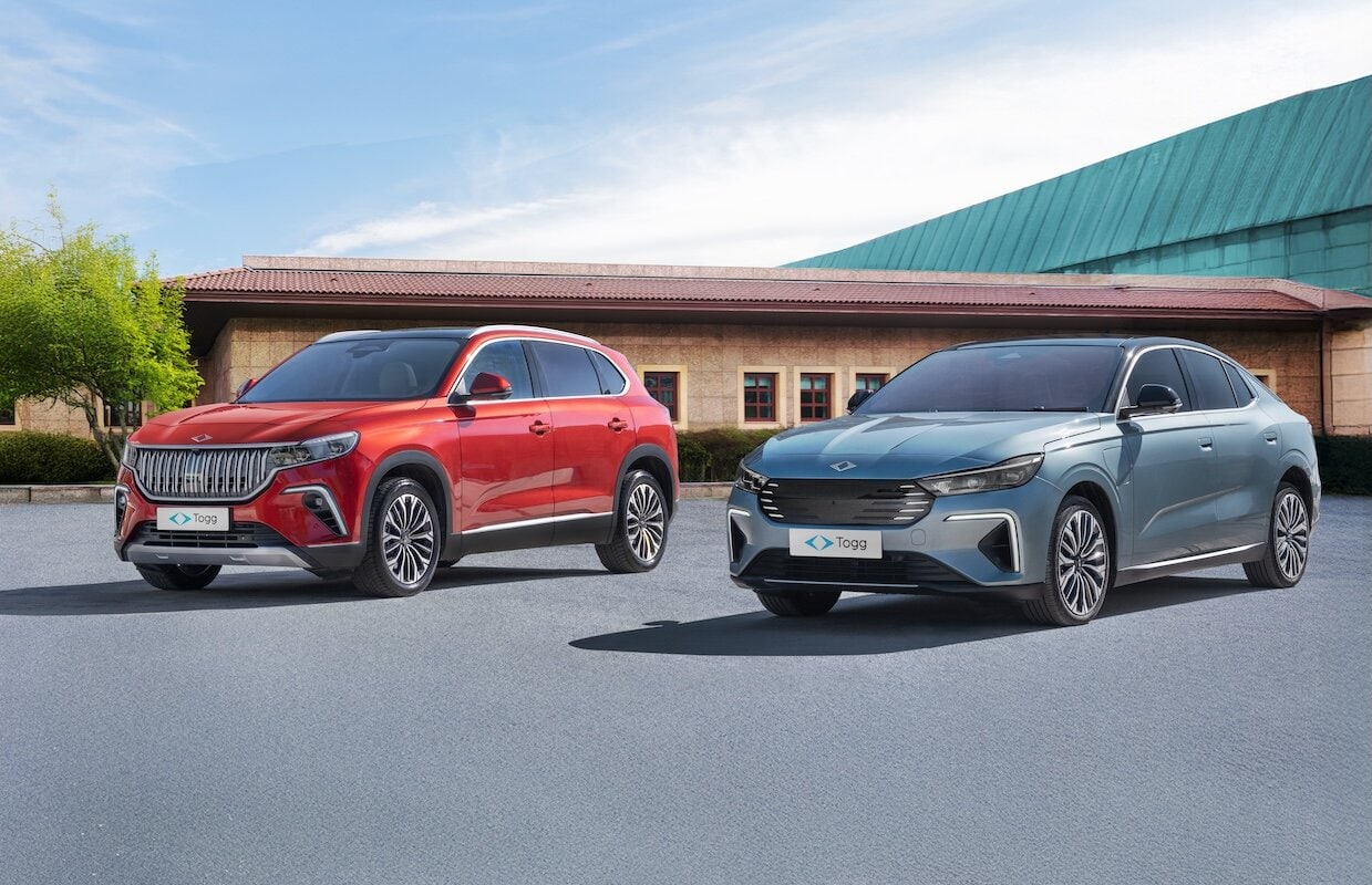 Due auto elettriche Togg parcheggiate fianco a fianco su una superficie asfaltata. A sinistra il SUV rosso Togg T10X con griglia cromata, a destra la berlina blu Togg T10F