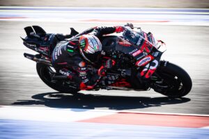 Marco Bezzecchi in MotoGP su moto Aprilia in piega durante una curva, con livrea nera e rossa e casco aerodinamico.