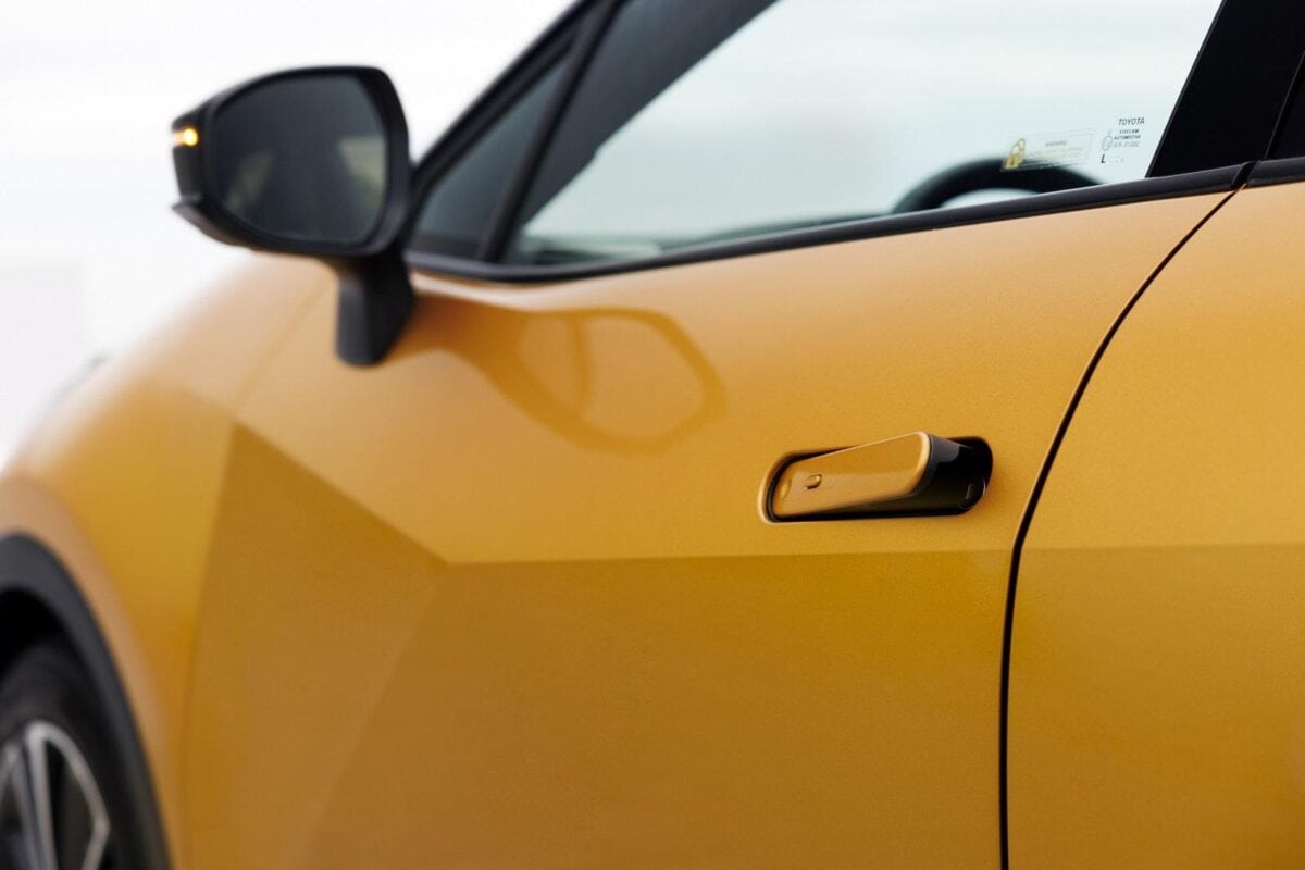 Dettaglio della maniglia a scomparsa della portiera di una Toyota c-hr gialla, vista ravvicinata con specchietto laterale e parte del finestrino anteriore.