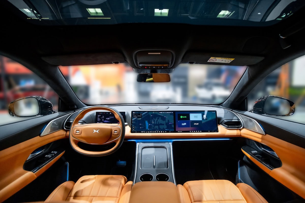 Vista dell’abitacolo del XPeng P7 con interni in pelle marrone e ampia plancia digitale con tre schermi continui, che integrano infotainment, navigazione e comandi.