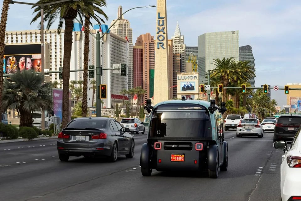 Il robotaxi Zoox attraversa la Strip di Las Vegas, con i casinò e gli hotel iconici sullo sfondo, tra traffico urbano e semafori.